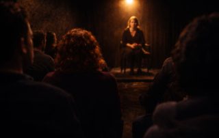 Intimate black box theatre performance with audience seated close to a performer under warm spotlight at Edinburgh Fringe Festival 2026