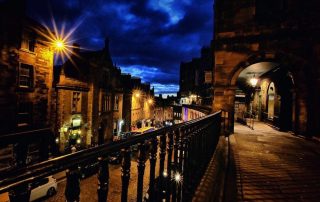 Edinburgh Old Town at night during the Fringe, with warm streetlights glowing over historic buildings and cobblestone streets